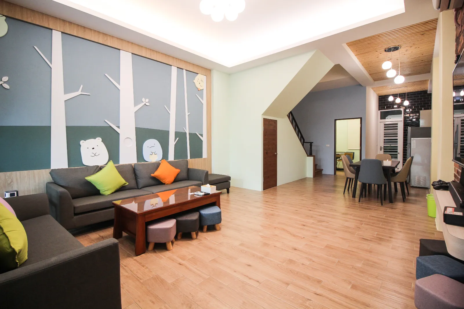 一樓包棟大廳客廳與餐桌空間，灰色沙發搭配森林主題牆面